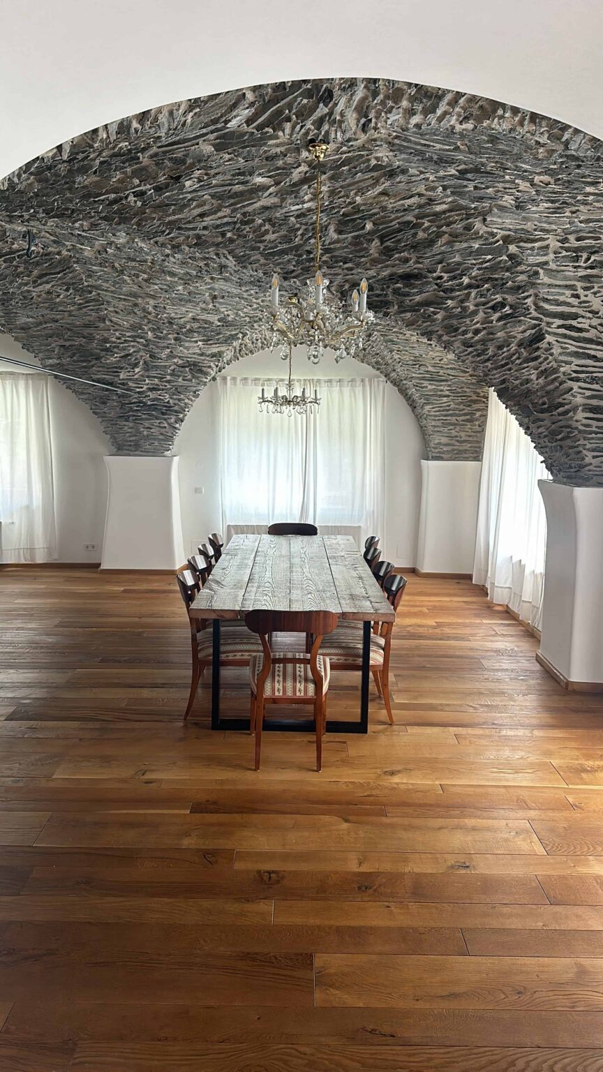 Esstisch mit rustikaler Holzplatte und schwarzen Tischkufen in historischem Raum mit Steinbogen-Decke