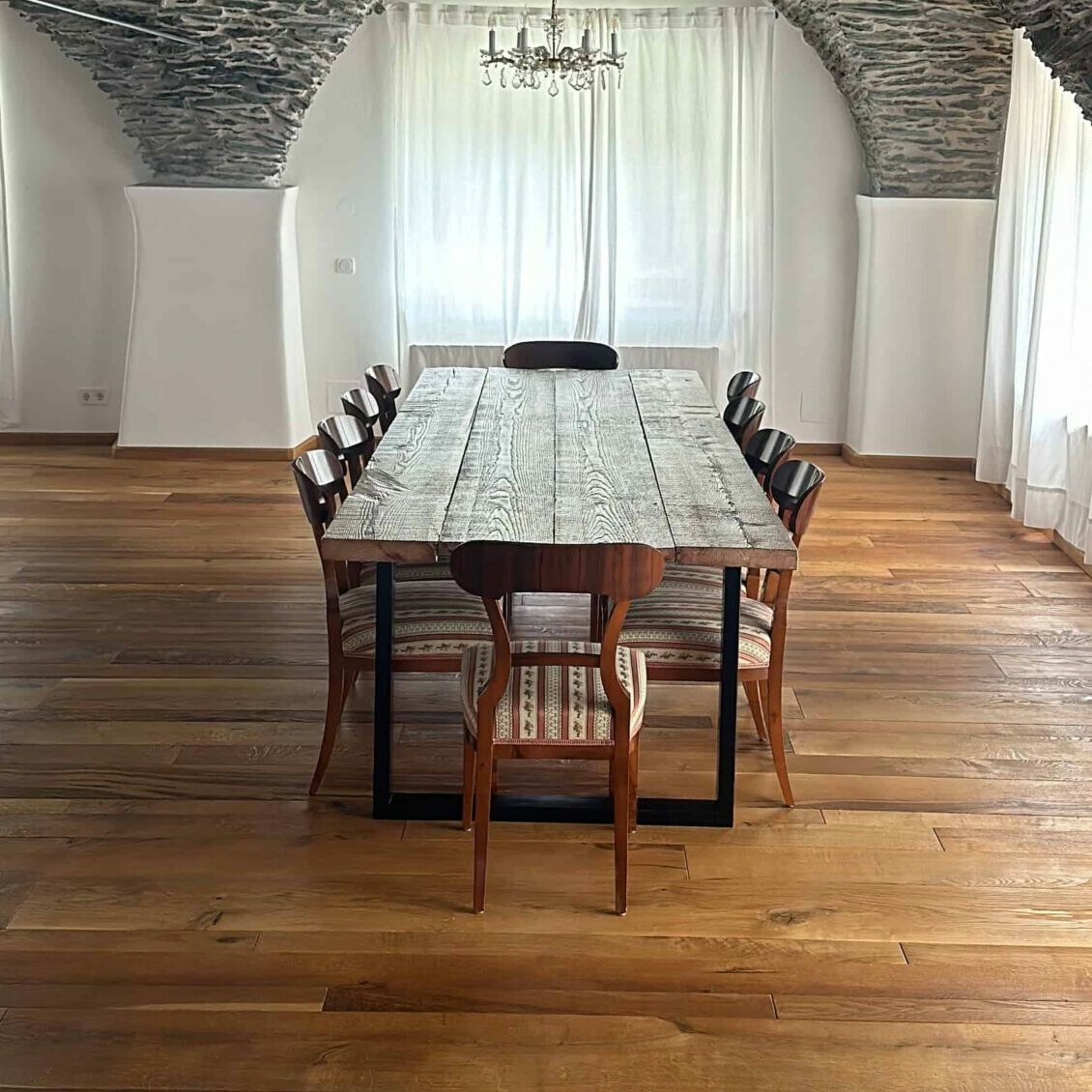 Esstisch mit rustikaler Holzplatte und schwarzen Tischkufen in historischem Raum mit Steinbogen-Decke